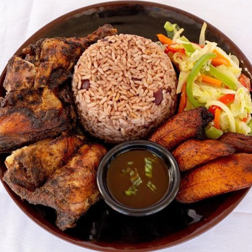 Ms. Martha's Caribbean Kitchen jerk chicken with rice, plantains, and coleslaw on a brown plate.