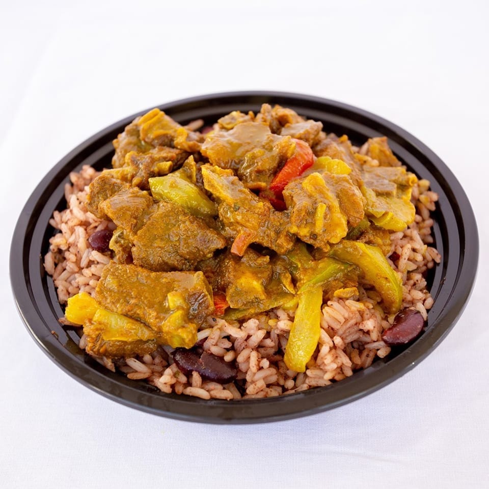 Ms. Martha's Caribbean Kitchen curry goat with rice and peas in a black bowl.